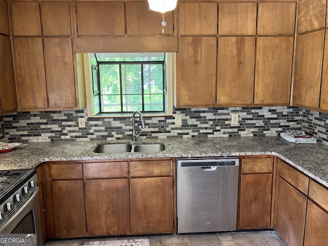 kitchen with brown cabinetry, decorative backsplash, stone countertops, a sink, and appliances with stainless steel finishes