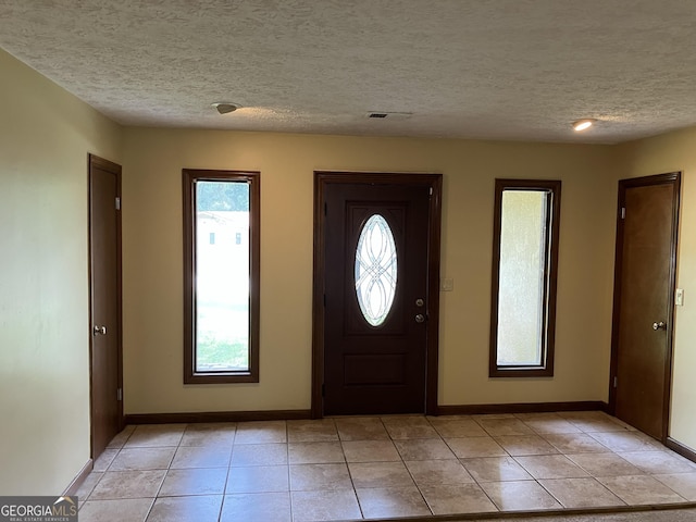 entryway featuring baseboards, light tile patterned flooring, a textured ceiling, and visible vents
