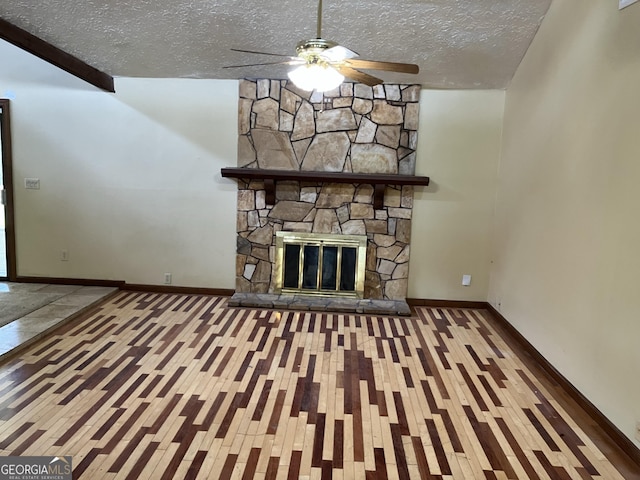 unfurnished living room with ceiling fan, a stone fireplace, a textured ceiling, wood finished floors, and baseboards