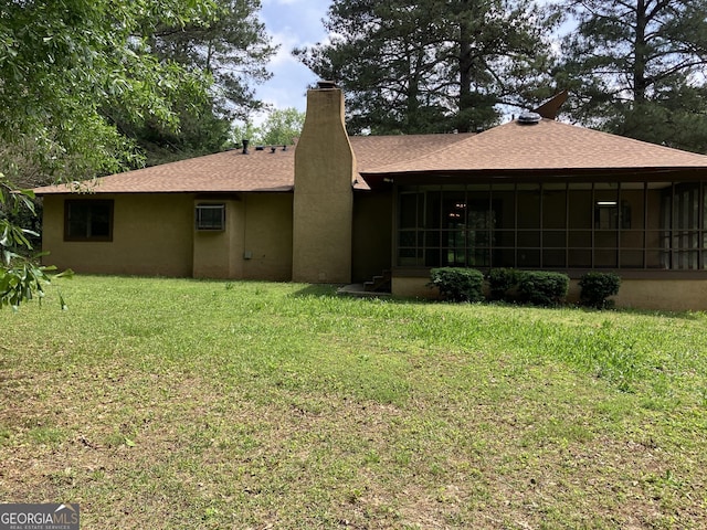 back of house featuring a sunroom, roof with shingles, a lawn, and stucco siding
