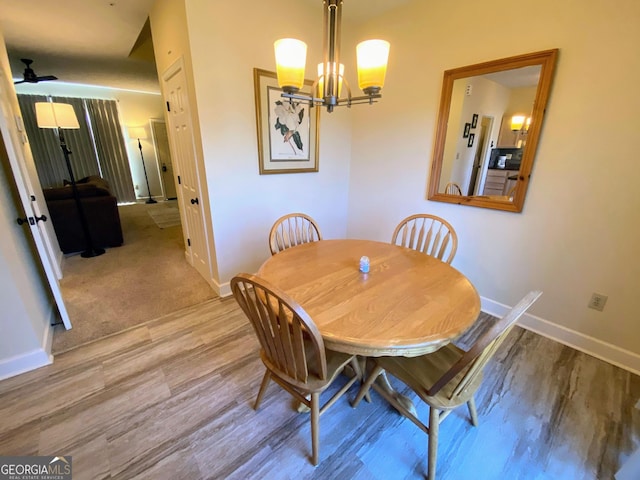 dining space featuring ceiling fan with notable chandelier, baseboards, and wood finished floors