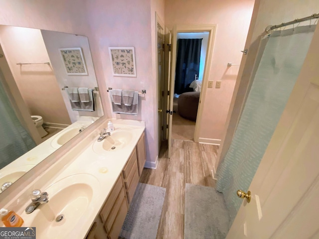 ensuite bathroom with baseboards, a sink, and wood finished floors