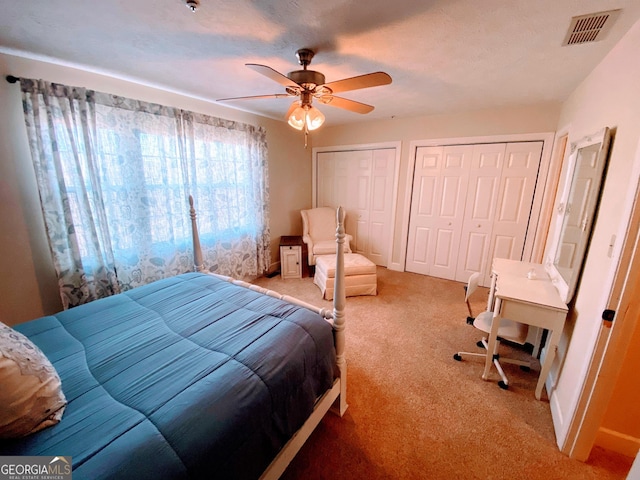 bedroom featuring light colored carpet, baseboards, multiple closets, ceiling fan, and visible vents