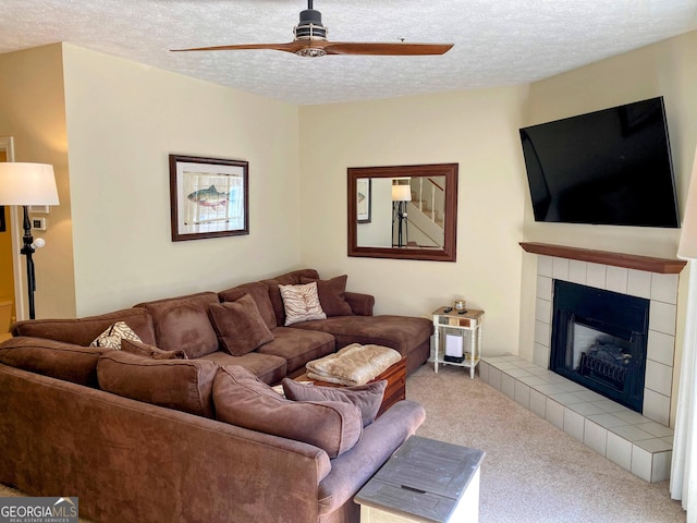 living area featuring carpet flooring, a ceiling fan, a tiled fireplace, and a textured ceiling