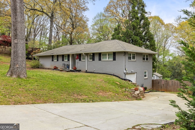 ranch-style house featuring a front yard, concrete driveway, an attached garage, fence, and brick siding