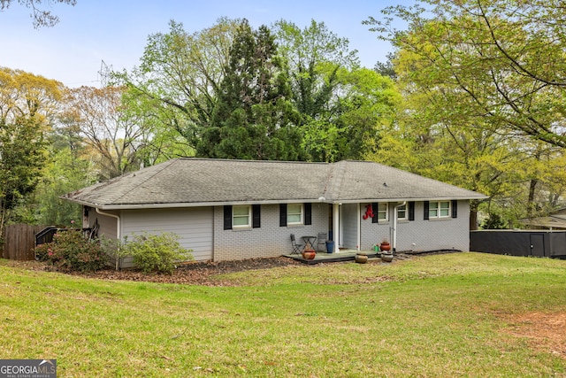 ranch-style house with brick siding, fence, roof with shingles, and a front yard