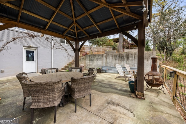 view of patio featuring fence, stairs, outdoor dining area, a gazebo, and a fire pit