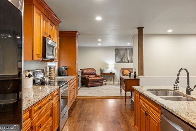 kitchen with light stone counters, a sink, dark wood finished floors, brown cabinets, and stainless steel appliances
