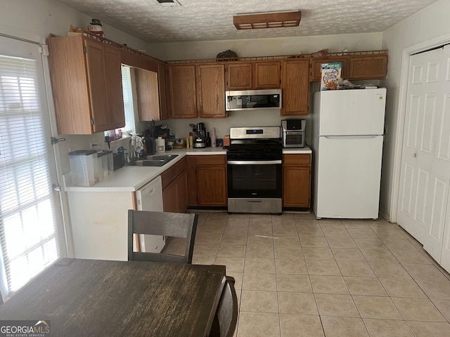 kitchen featuring a sink, appliances with stainless steel finishes, brown cabinetry, light countertops, and light tile patterned floors