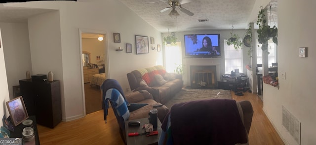 living area featuring a fireplace, wood finished floors, visible vents, and ceiling fan