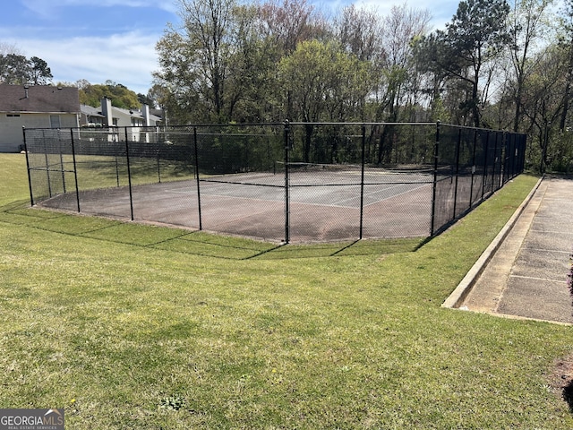 view of tennis court featuring fence and a yard