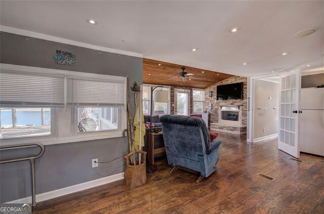 living room featuring wood finished floors, vaulted ceiling, a stone fireplace, ceiling fan, and baseboards