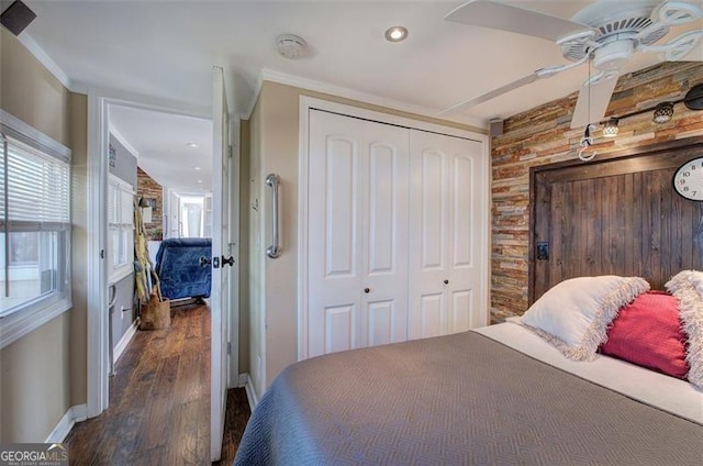 bedroom featuring a closet, wood finished floors, crown molding, baseboards, and an accent wall