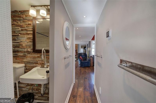 corridor featuring wood finished floors, a sink, baseboards, and ornamental molding