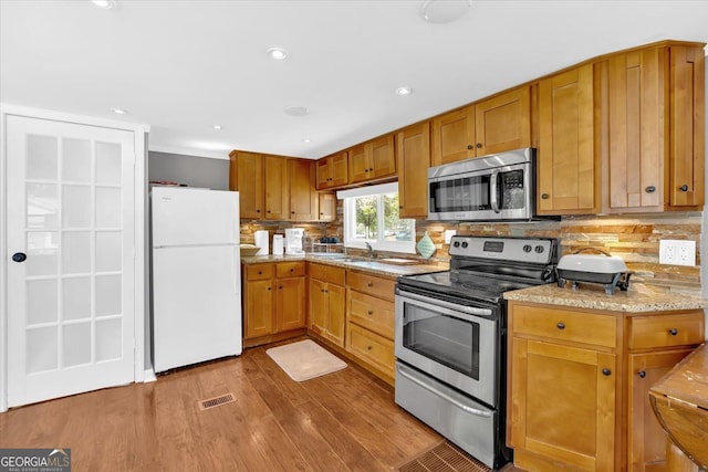kitchen featuring stainless steel appliances, wood finished floors, decorative backsplash, a sink, and recessed lighting