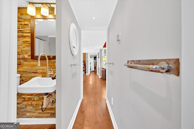 corridor featuring a sink, wood finished floors, baseboards, and ornamental molding