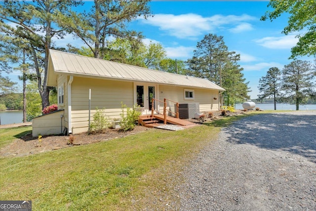 view of front of home featuring a water view, metal roof, a front yard, gravel driveway, and french doors