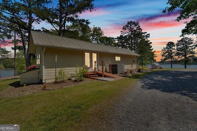 view of front facade featuring metal roof, a yard, driveway, and a water view