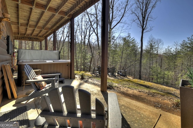 view of patio / terrace featuring a view of trees and a hot tub
