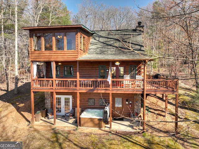 back of property with a wooden deck, faux log siding, a hot tub, french doors, and a patio area