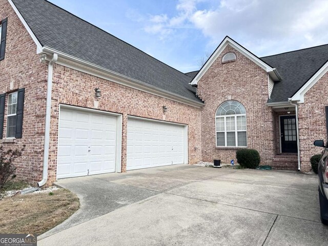 view of property exterior with a shingled roof, brick siding, and driveway