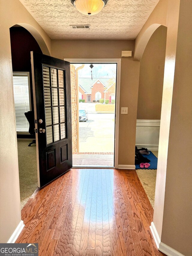 foyer entrance with arched walkways, wood finished floors, and baseboards