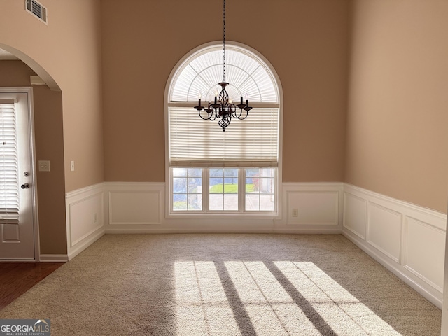 unfurnished dining area with arched walkways, carpet flooring, a wainscoted wall, a chandelier, and a decorative wall