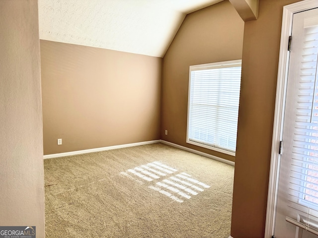 carpeted spare room featuring lofted ceiling and baseboards