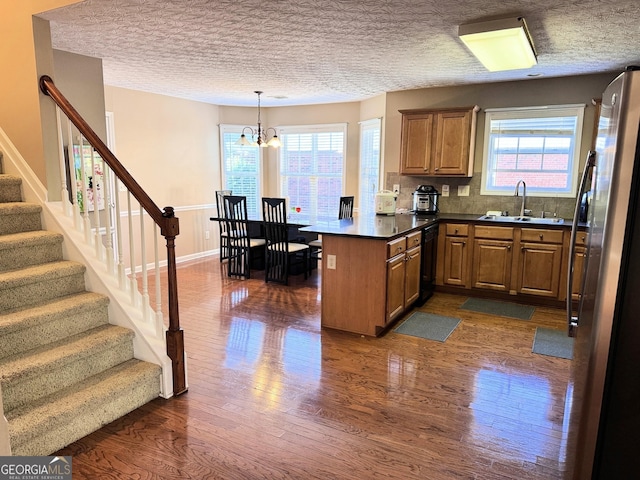 kitchen with freestanding refrigerator, dishwasher, a sink, a peninsula, and dark wood finished floors