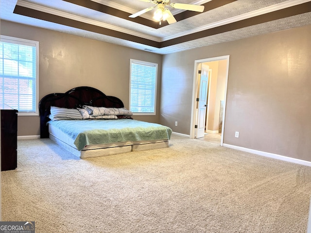 carpeted bedroom featuring a raised ceiling, ornamental molding, multiple windows, baseboards, and a ceiling fan