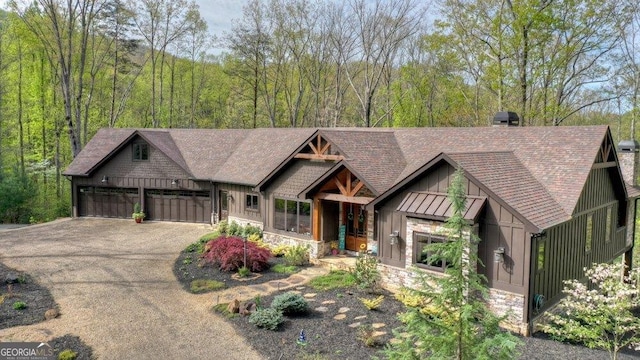 view of front of property featuring driveway, stone siding, roof with shingles, an attached garage, and board and batten siding