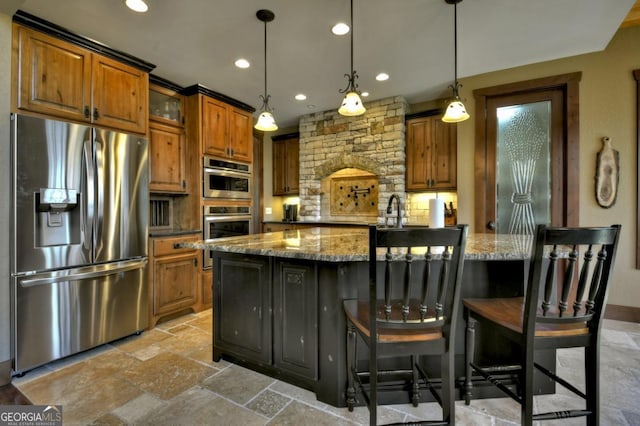 kitchen featuring backsplash, light stone counters, stone tile flooring, appliances with stainless steel finishes, and brown cabinetry