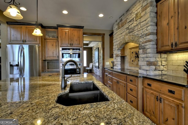 kitchen featuring stainless steel appliances, backsplash, dark stone counters, a sink, and glass insert cabinets