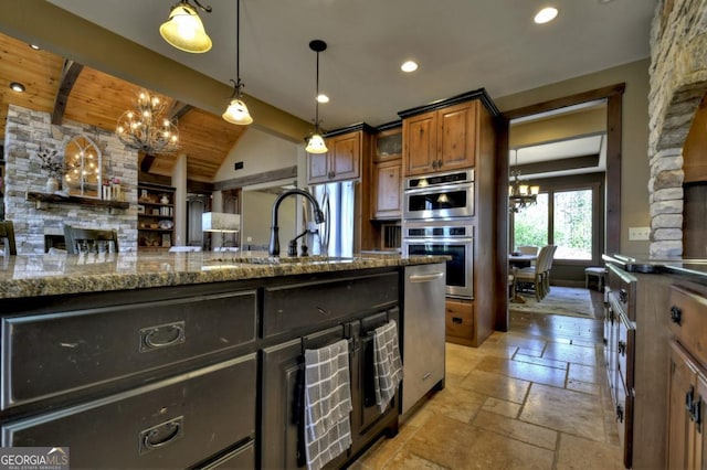 kitchen with stainless steel appliances, a sink, stone countertops, an inviting chandelier, and stone tile floors