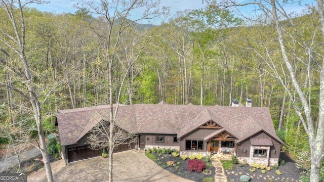 craftsman-style house with stone siding, a chimney, a shingled roof, and a forest view