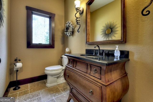 bathroom featuring baseboards, vanity, toilet, and stone tile flooring