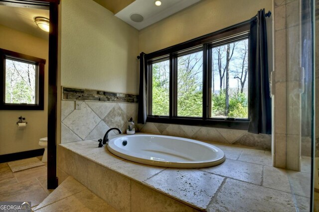 full bath featuring toilet, stone tile flooring, and a bath