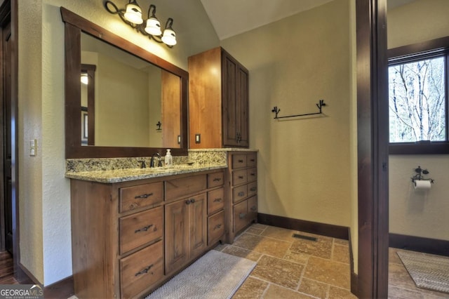 bathroom featuring visible vents, baseboards, vanity, stone tile flooring, and a textured wall
