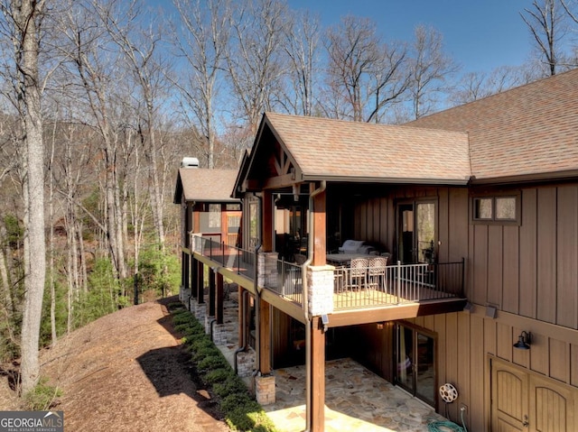 exterior space with a shingled roof, board and batten siding, a deck, and a patio area