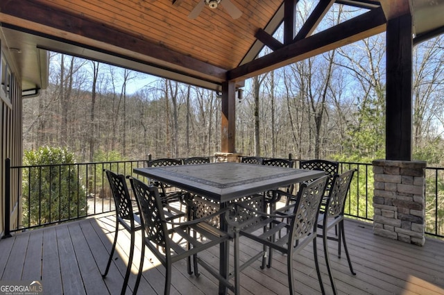 wooden terrace with outdoor dining space, ceiling fan, and a forest view
