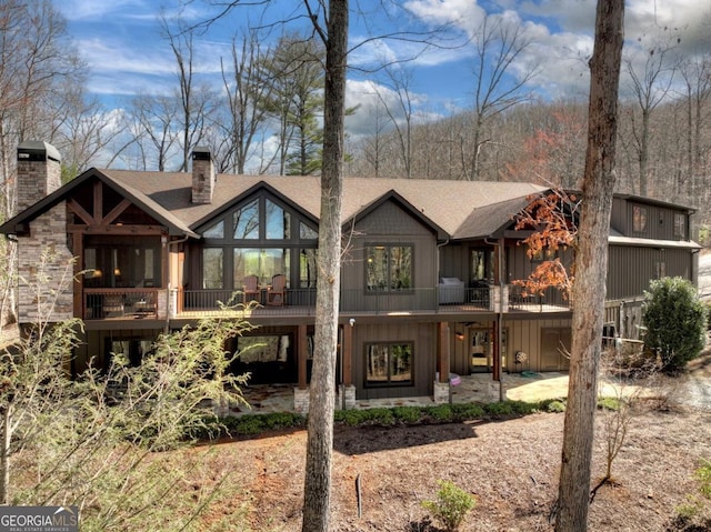 rear view of property with a patio, a chimney, and roof with shingles