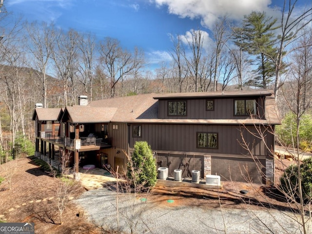 exterior space featuring stone siding, roof with shingles, a deck, and a chimney