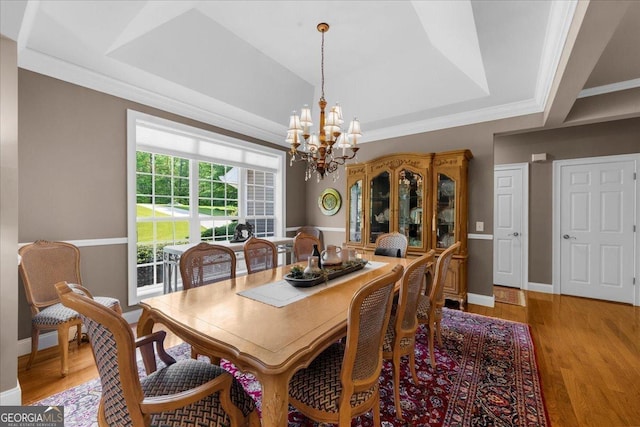 dining area featuring a raised ceiling, baseboards, light wood finished floors, a chandelier, and ornamental molding
