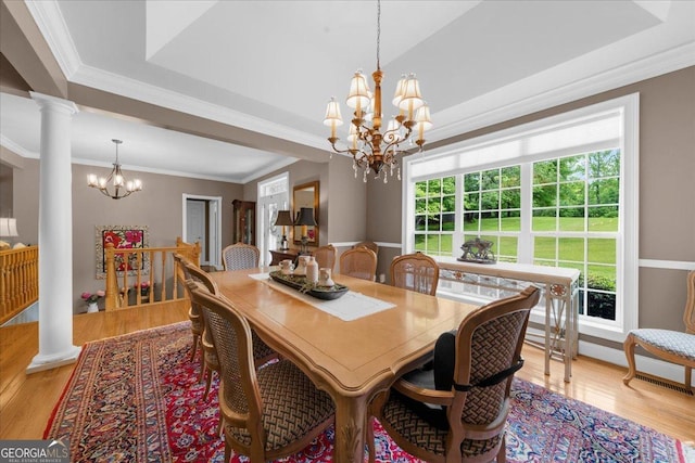 dining area featuring crown molding, an inviting chandelier, light wood finished floors, ornate columns, and a tray ceiling