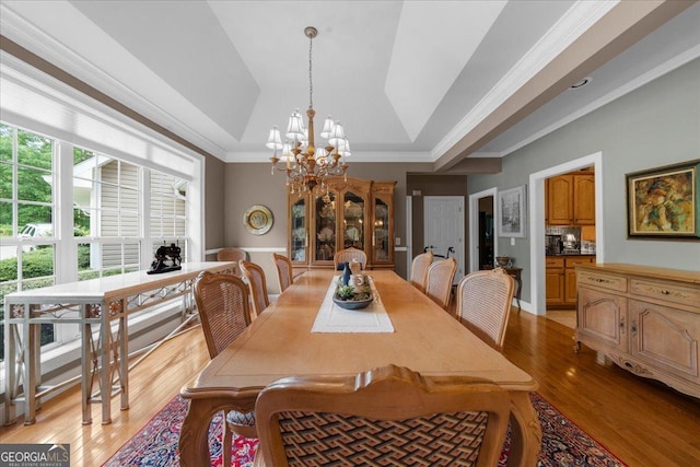 dining area featuring crown molding, light wood finished floors, a tray ceiling, and a notable chandelier