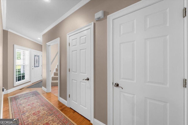 entryway with crown molding, baseboards, stairway, and light wood-style floors