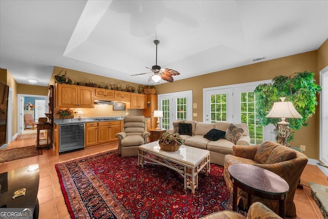 living area with wine cooler, light tile patterned floors, ceiling fan, and a tray ceiling