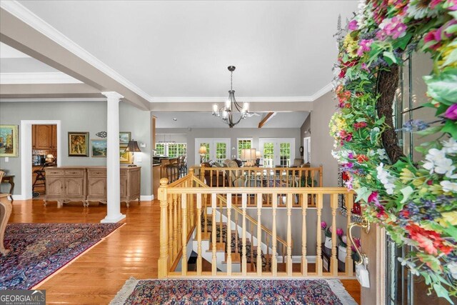 interior space featuring an inviting chandelier, crown molding, ornate columns, and wood finished floors