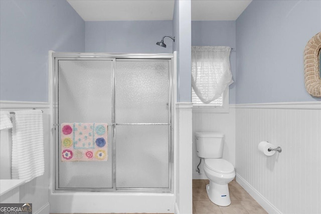 bathroom featuring tile patterned flooring, a wainscoted wall, toilet, and a shower stall