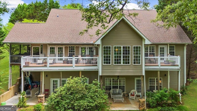 back of property featuring a shingled roof, a patio area, and a balcony